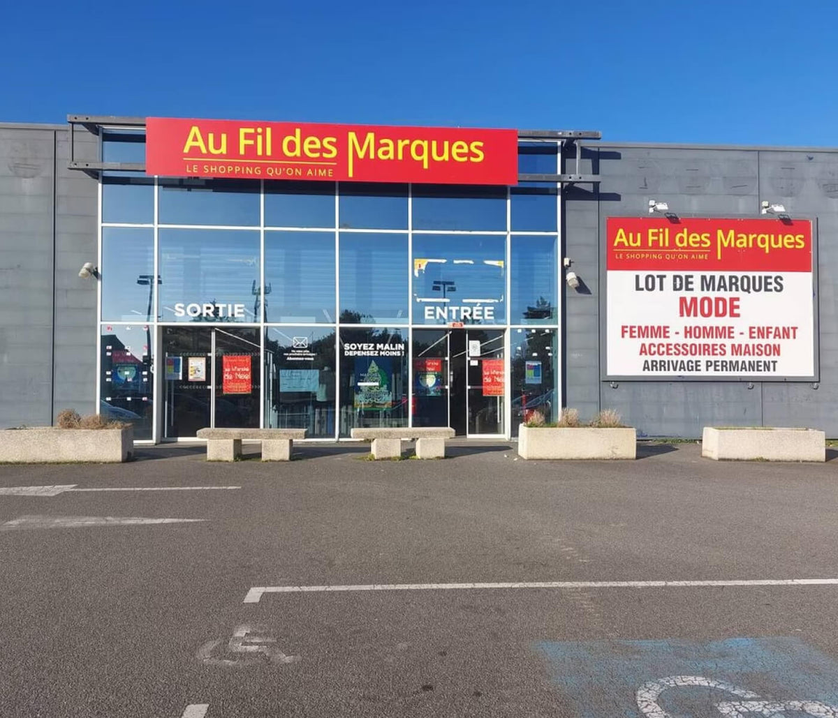 Façade d'un magasin Au Fil des Marques et son parking